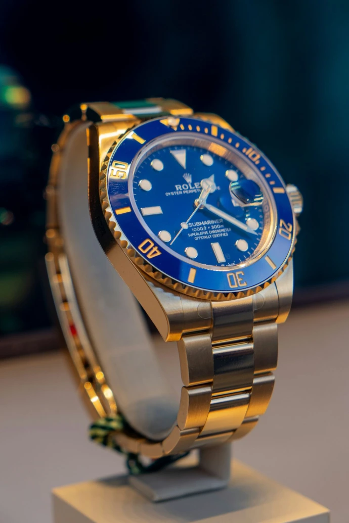 A blue and gold rolex watch on a stand
